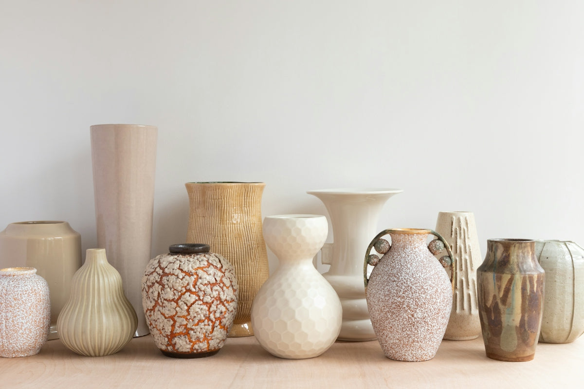 A collection of various ceramic vases in neutral tones on a wooden surface
